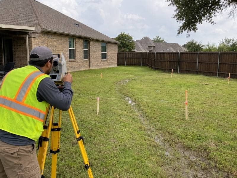 Drainage surveyor measuring yard elevations for an ADU project in Grand Prairie Texas
