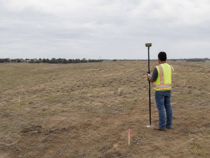 Elevation surveyor collecting GPS grade measurements on a sloped building lot in Grand Prairie Texas